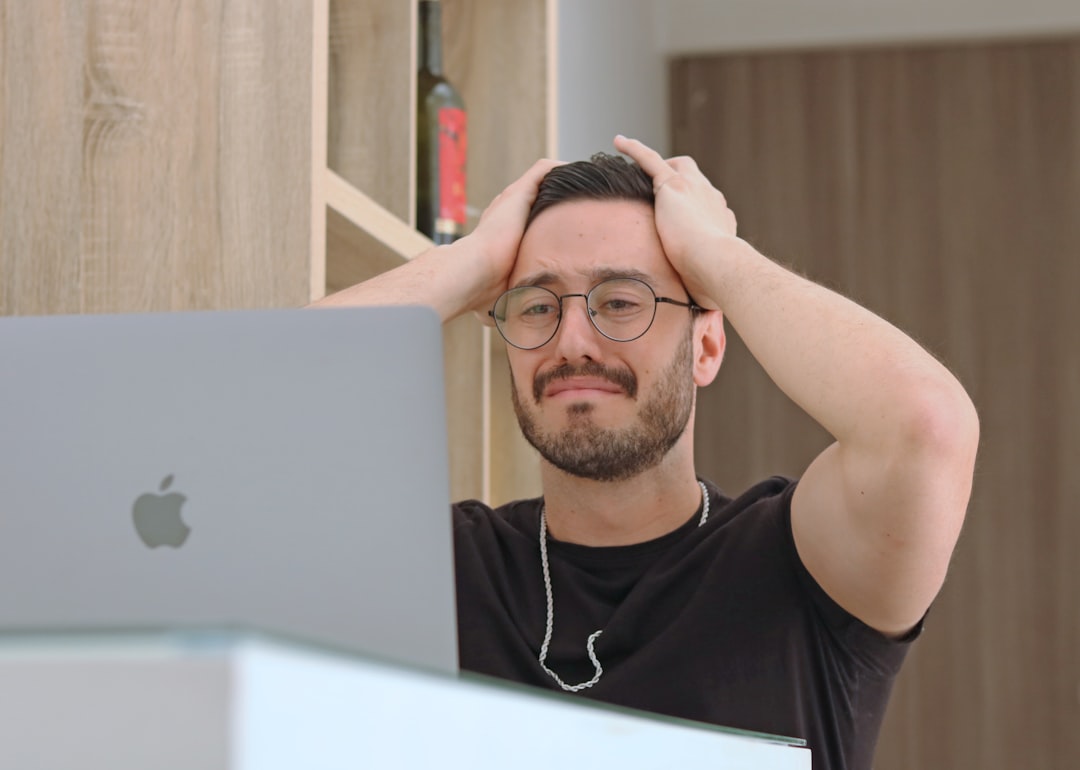 a man with glasses is looking at a laptop stressed